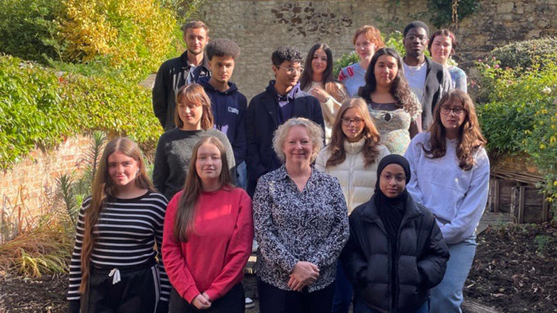 Group photo taken in an outdoor garden setting with stone walls and greenery in the background. The image shows new Astrophoria Foundation Year students for the 2025/26 cohort standing on wooden steps alongside Dr Alison MacDonald, under a clear blue sky.