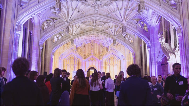 Picture of a crowd of guests inside the Divinity School, bathed in purple light