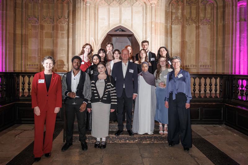Group portrait taken in the Divinity School, Oxford. The Vice-Chancellor of Oxford stands on the far left wearing a red suit, and the Chancellor stands at the centre in a dark suit. At the right is the Director of the Astrophoria Foundation Year