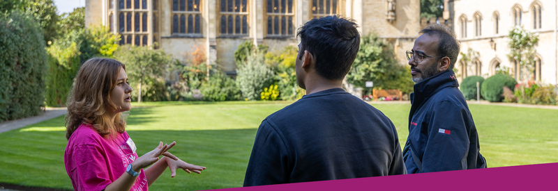 Photo of an Oxford University student ambassador talking to a prospective applicant and parent on a sunny college lawn