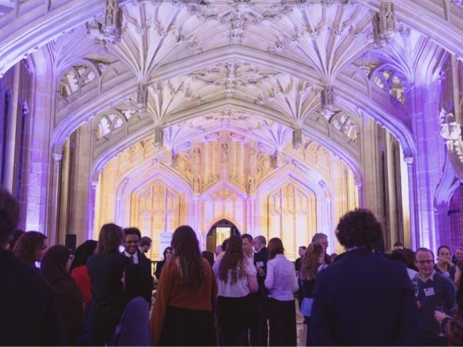 Picture of a crowd of guests inside the Divinity School, bathed in purple light