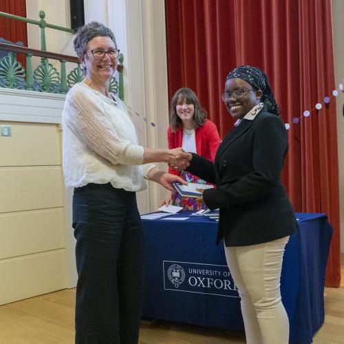 Dr Jo Begbie handing Foundation Year student Victoria a gift in the Simpkins Lee Theatre at Lady Margaret Hall