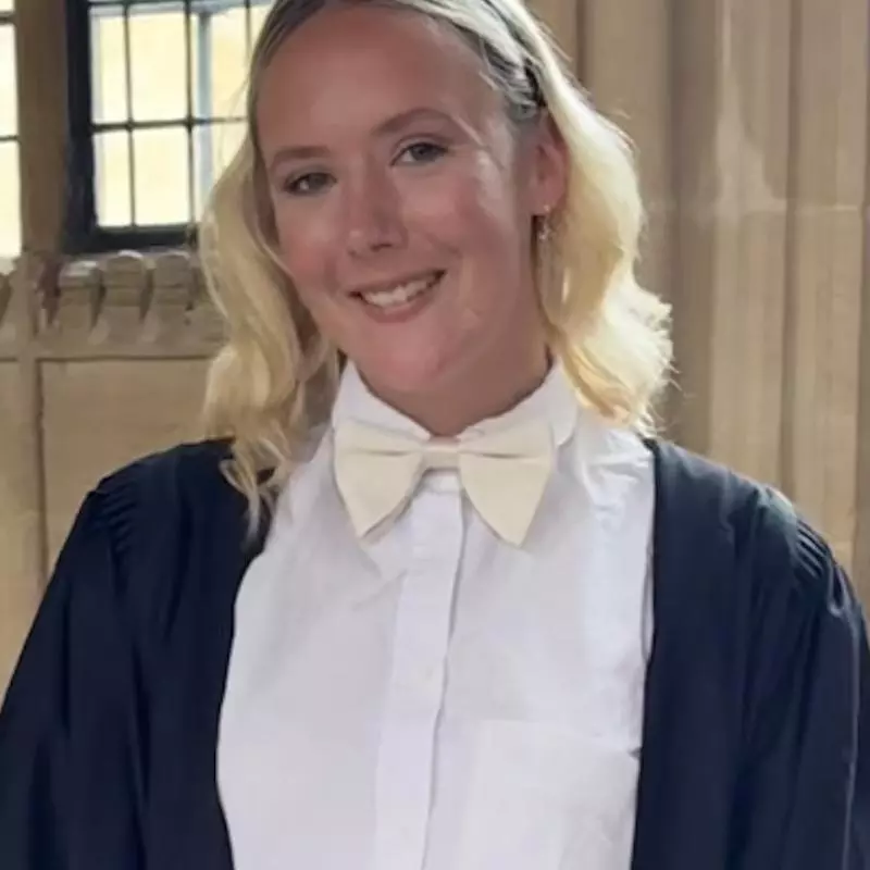 A young woman with blonde shoulder length hair wearing Oxford 'sub fusc' dress smiles at the camera