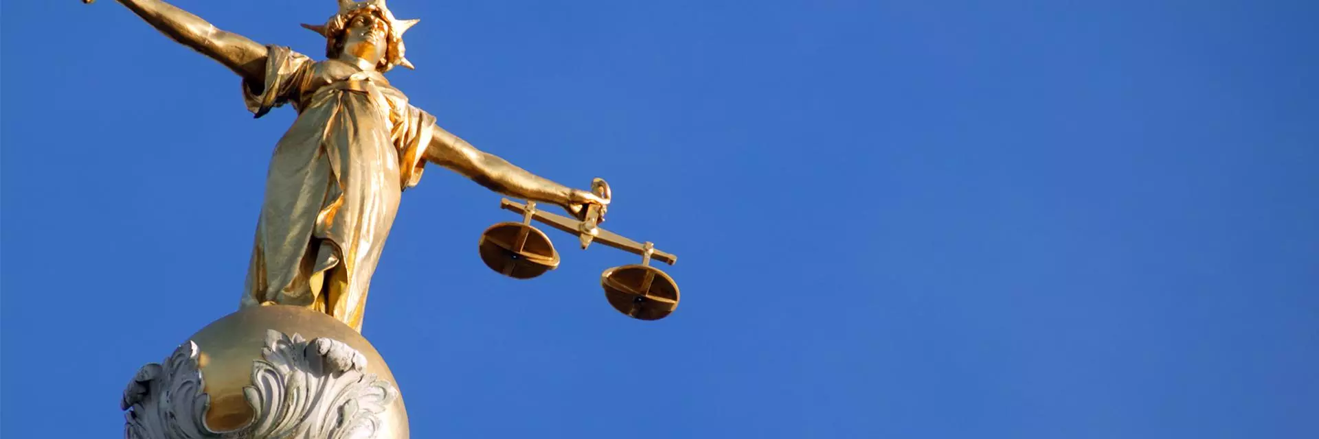 A picture of Lady Justice, a gold figure with arms outstretched holding a sword in one hand and scales in the other, against a clear blue sky